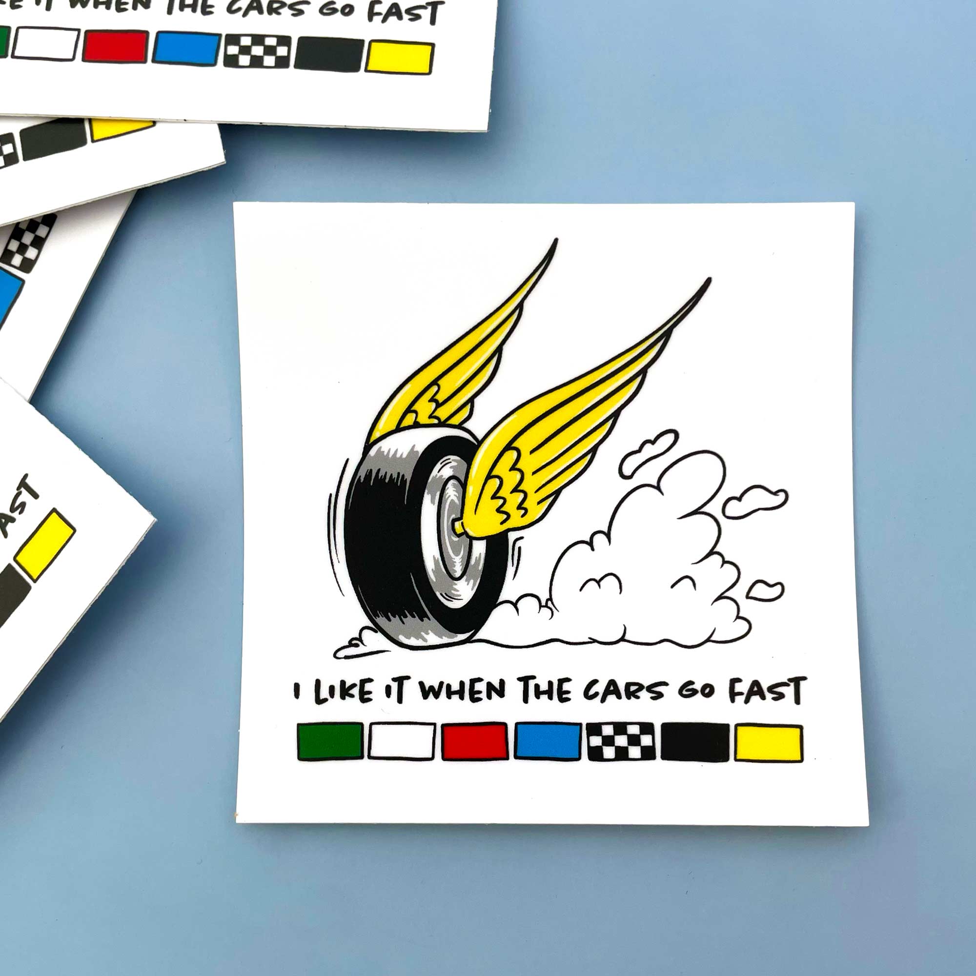 wing and wheel motor speedway cartoon graphic with text "I like it when the cars go fast" and the colors of the racing flags printed below on a white square sticker 