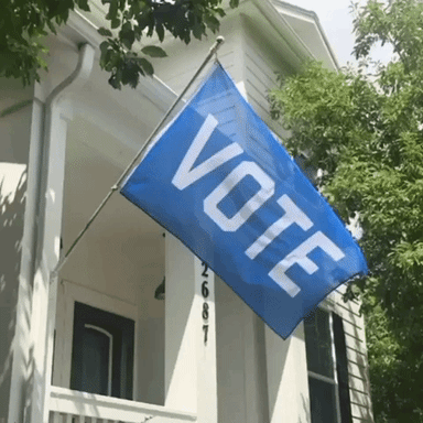 Blue flag with VOTE in white on a flagpole attached to a house waving back and forth as an animated gif.