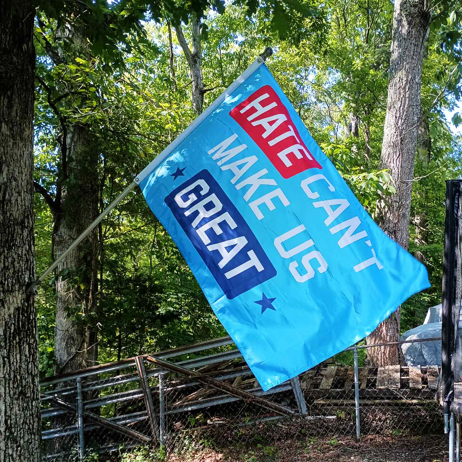"Hate Can't Make Us Great" blue flag on a flag pole on a tree