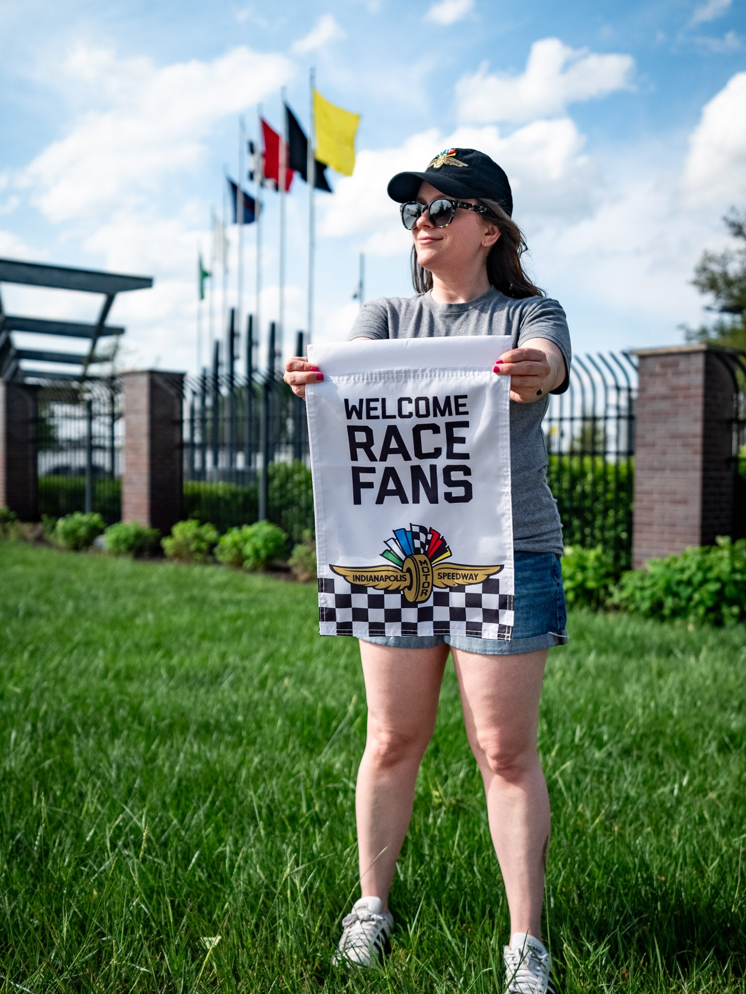 An Indianapolis Motor Speedway "Welcome Race Fans" garden flag being held by a woman.