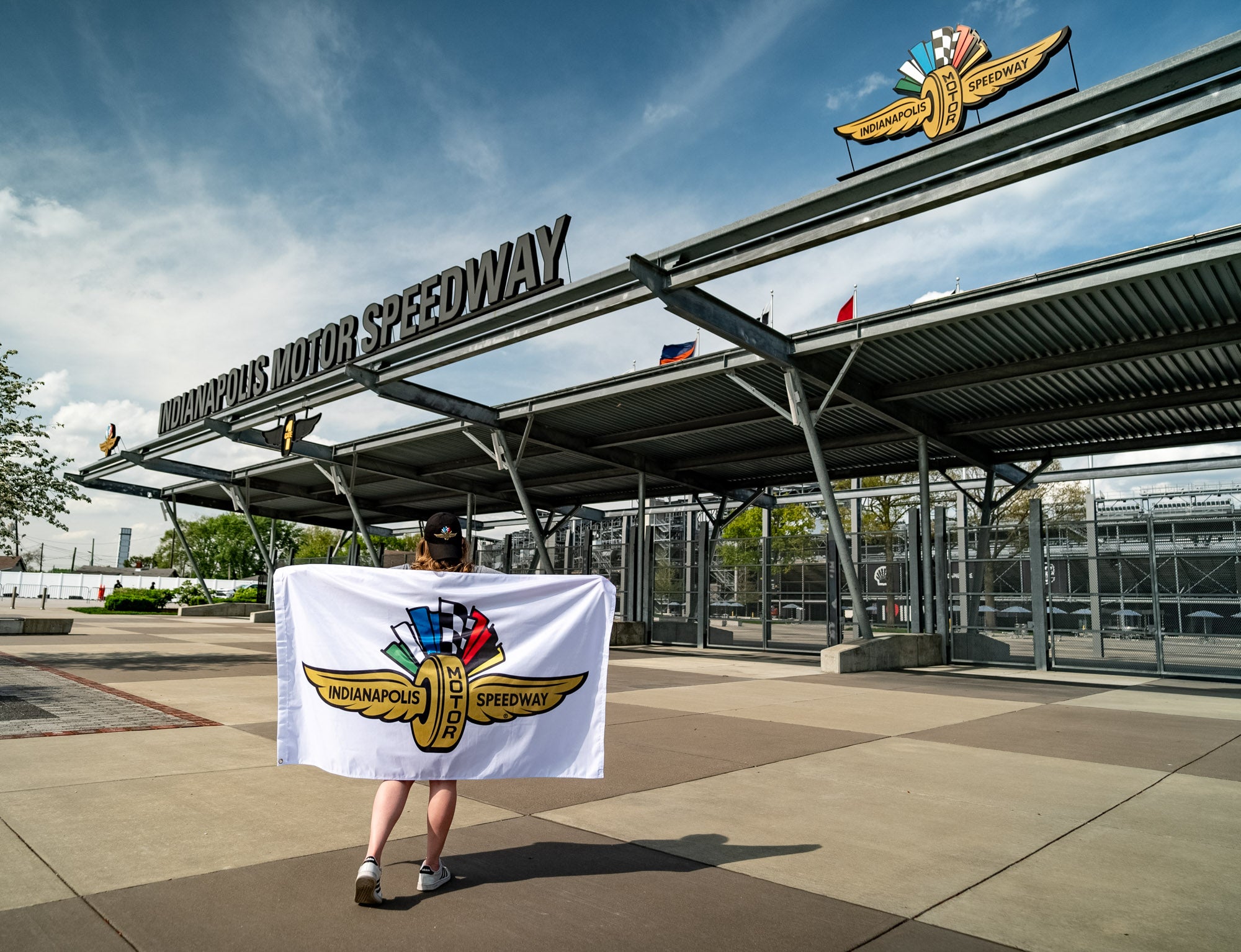An Indianapolis Motor Speedway logo flag being held by a woman walking into the IMS main gate.