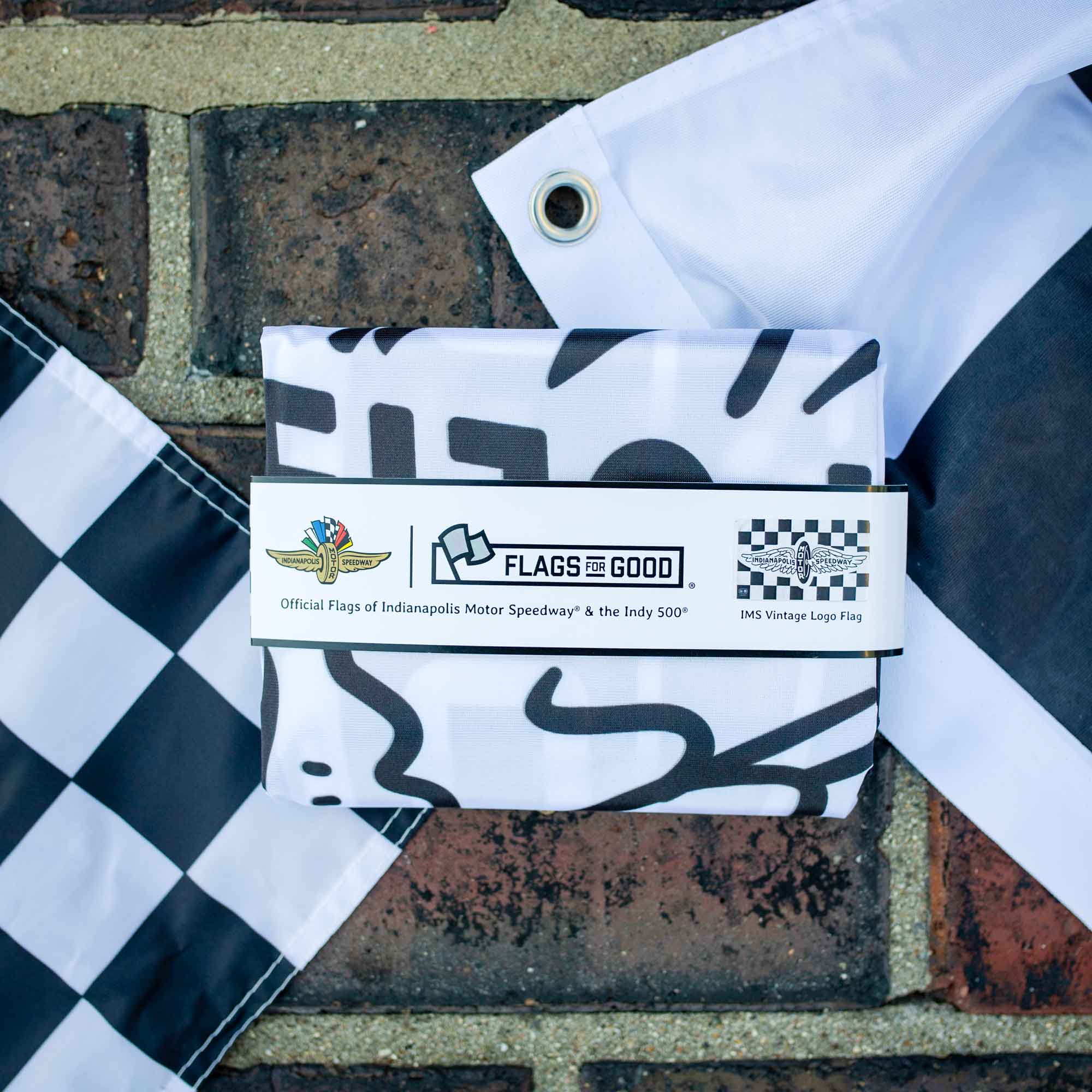 Packaged Indianapolis Motor Speedway Vintage black and white logo checkered flag with 'Flags For Good' label on the yard of bricks finish line at IMS