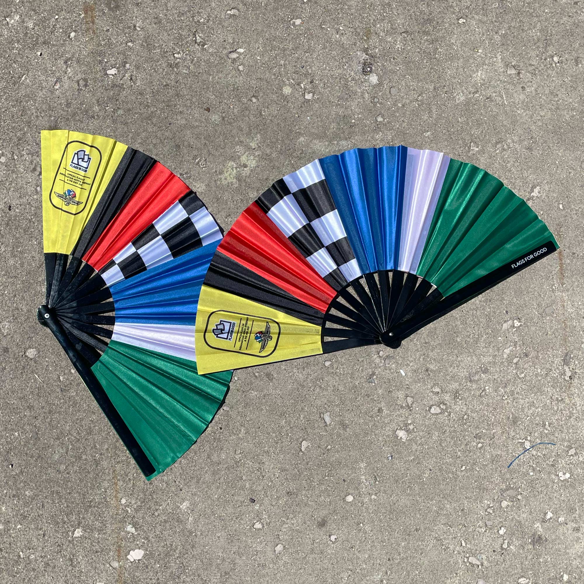 two cloth folding fan with bands of racing flag colors and a brand logo displayed on a concrete surface