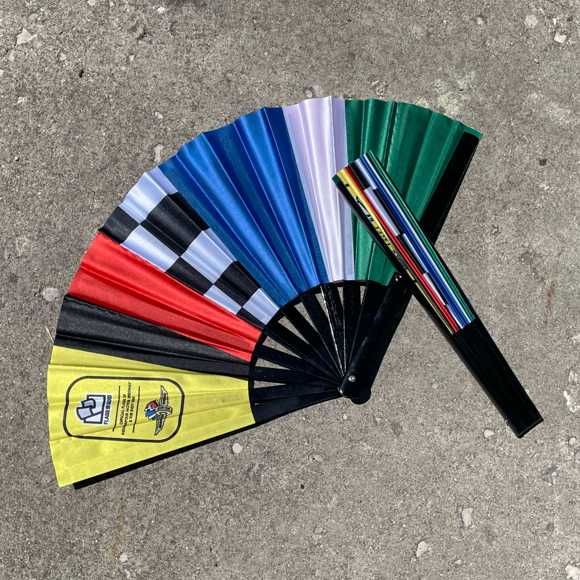 cloth folding fan with bands of racing flag colors and a brand logo displayed on a concrete surface