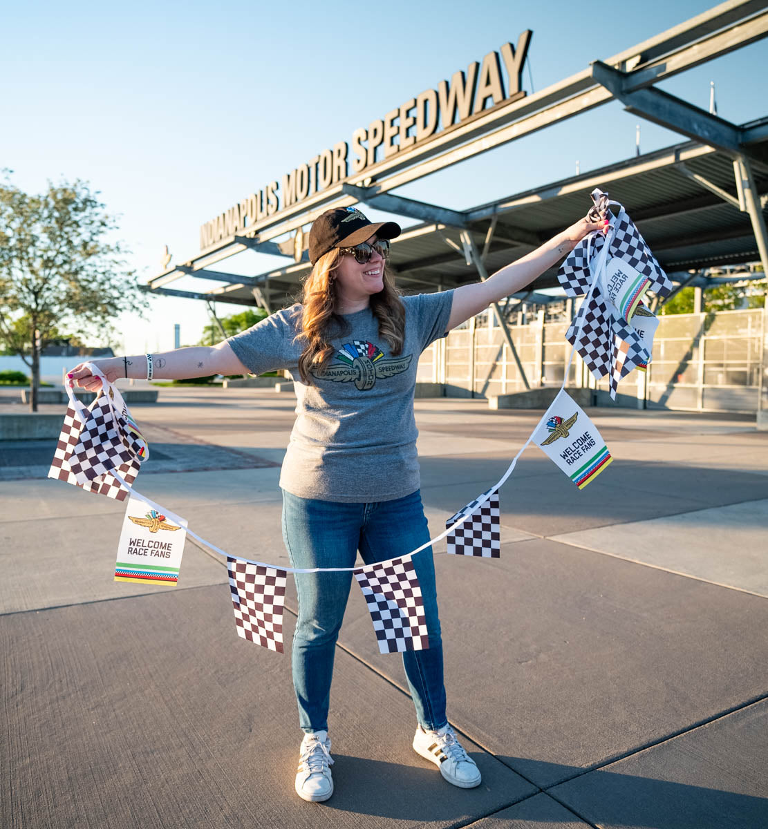 An Indianapolis Motor Speedway "Welcome Race Fans" checkered flag bunting being held by a woman in front of the IMS main gate.