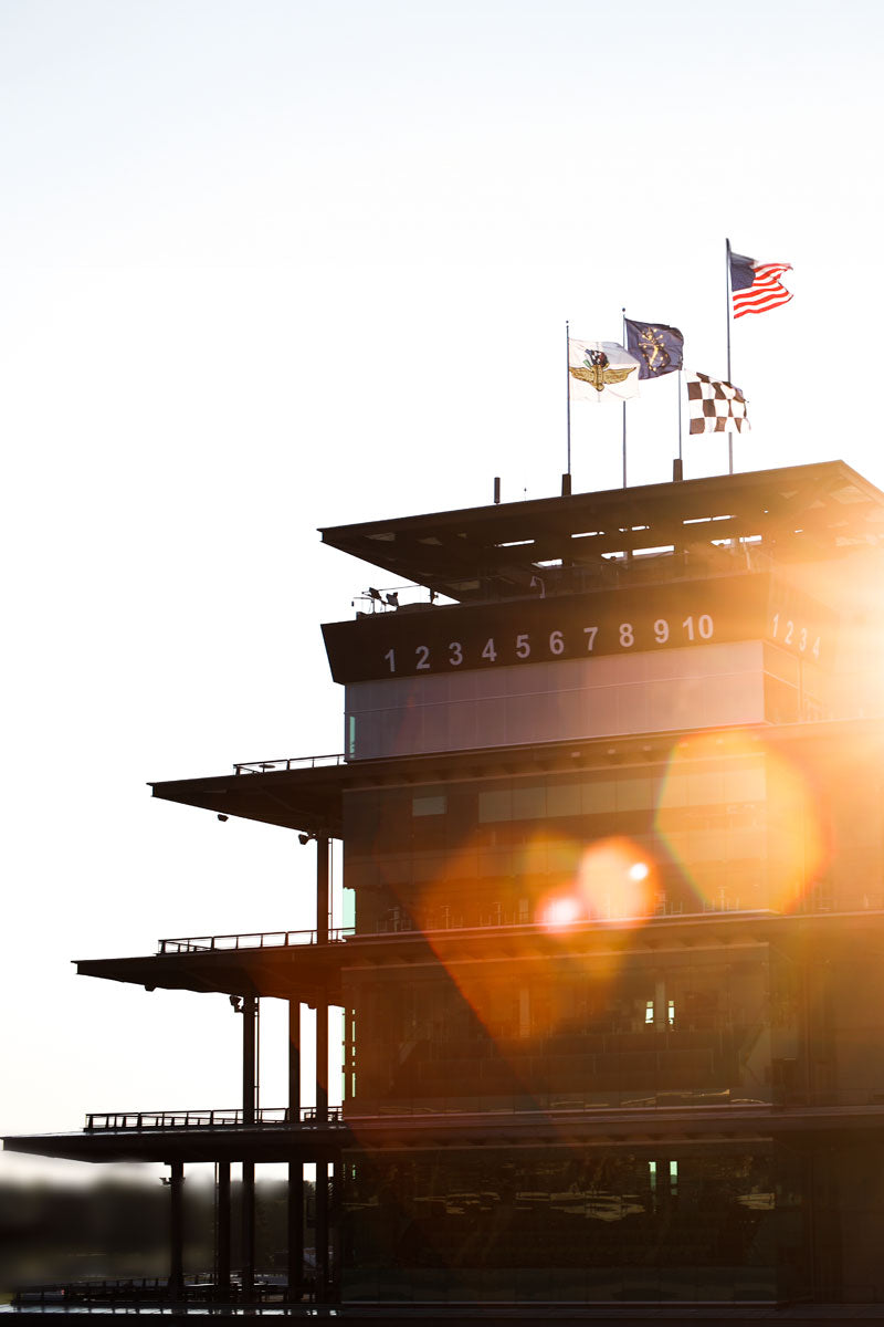Silhouette of the IMS Pagoda race track control tower with flags against a sunset sky.