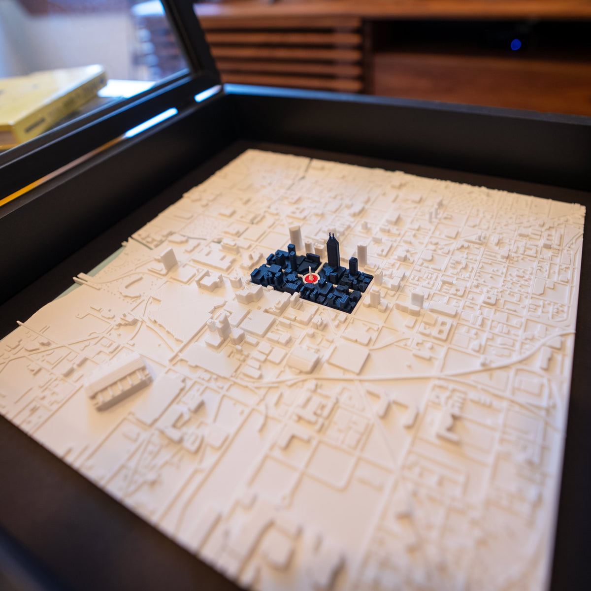 A 3D Indianapolis city map in cream-colored PLA, featuring the city flag as dark blue and red blocks showing the flag's overlay on the city grid displayed inside a premium openable black frame shadowbox.