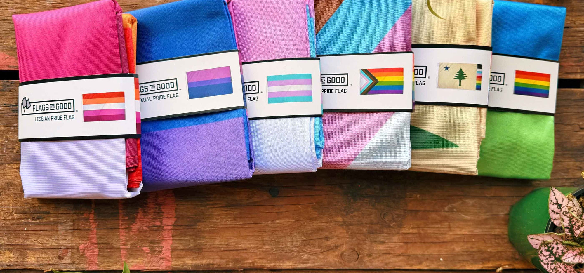 Colorful various lgbtq folded pride flags with Flags For Good brand labels on a wooden surface